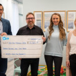 Four adults posing indoors while holding a giant charity check for $16,063 made out to Kristen French CACN, all smiling at the camera.