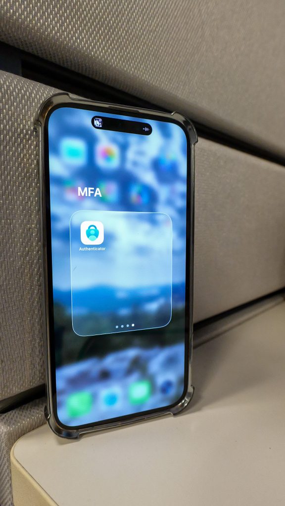 Close-up of a smartphone screen showing a folder labeled MFA and an Authenticator app icon on the home screen.