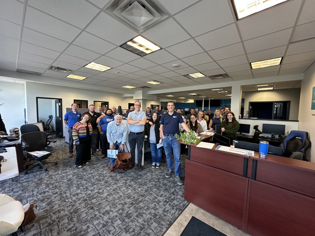 Group of coworkers standing together in an office lobby, smiling for a photo.
